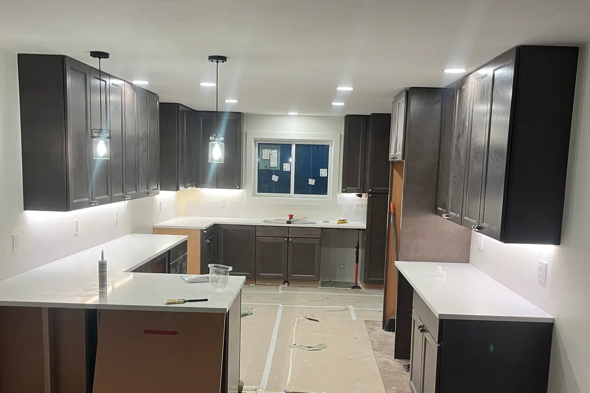 A finished U-shaped kitchen lit by mason-jar pendant lights, recessed cans, and under-cabinet LED lighting.