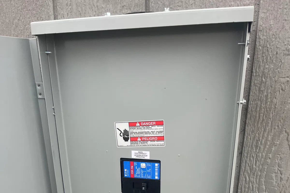An open exterior breaker panel with an Eaton main disconnect mounted on the gray siding of a home.