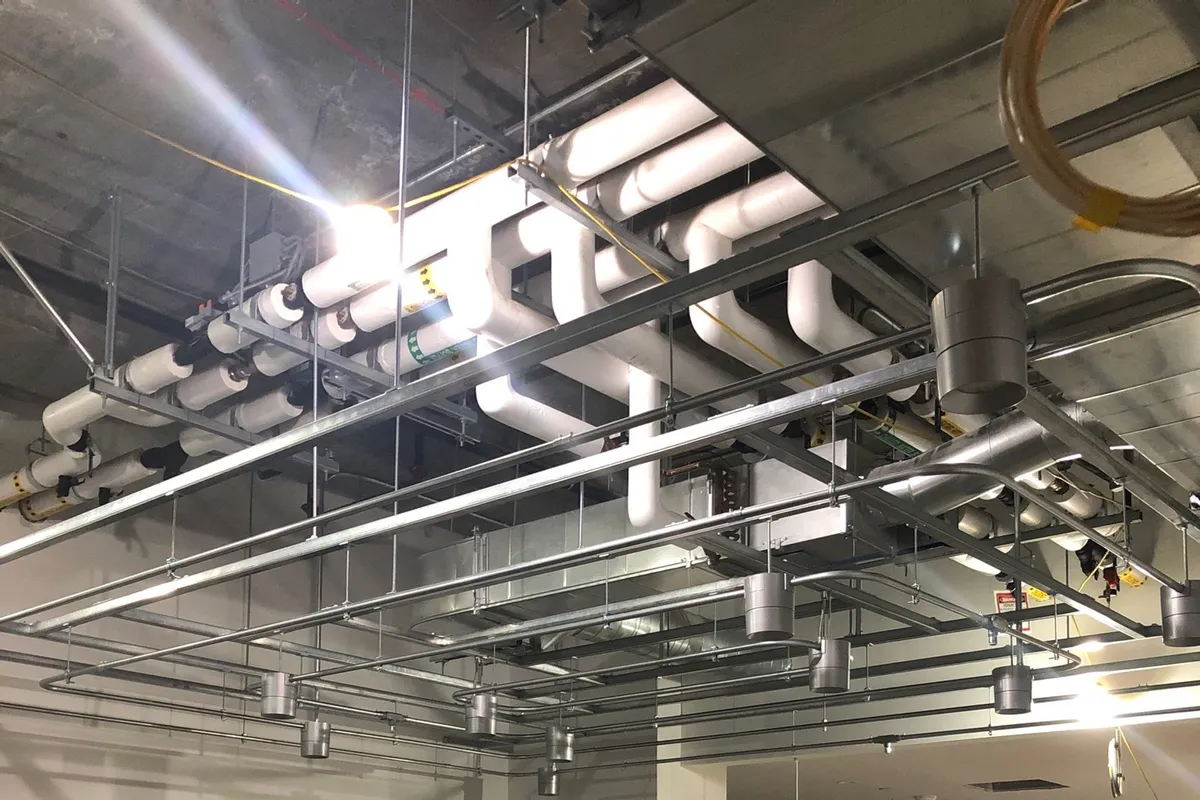A commercial tenant-improvement build-out with an extensive grid of EMT conduit feeding recessed light housings in an open structural ceiling.