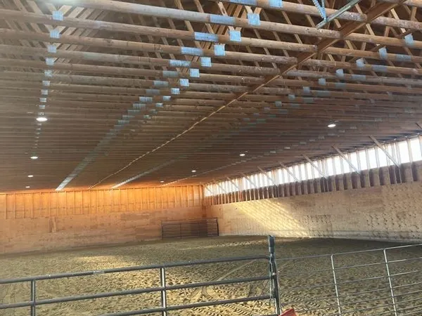 A large wood-truss indoor riding arena fitted with recessed high-bay lighting.