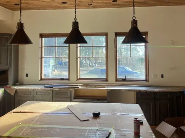 Three dark cone pendant lights over a kitchen island beneath a wood-plank ceiling.