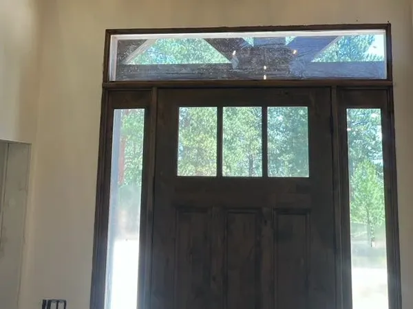 A rustic antler chandelier lit above a timber-and-glass front entry under a vaulted ceiling.