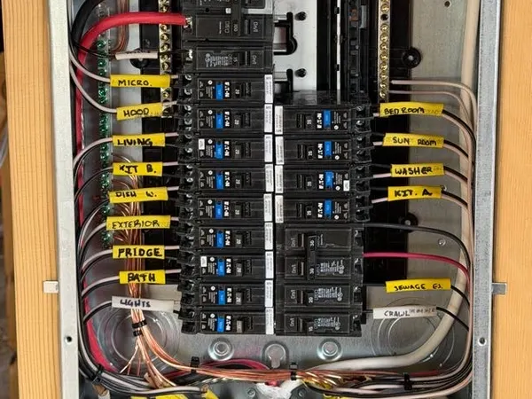 An open residential breaker panel with hand-labeled circuits and neatly landed wiring.
