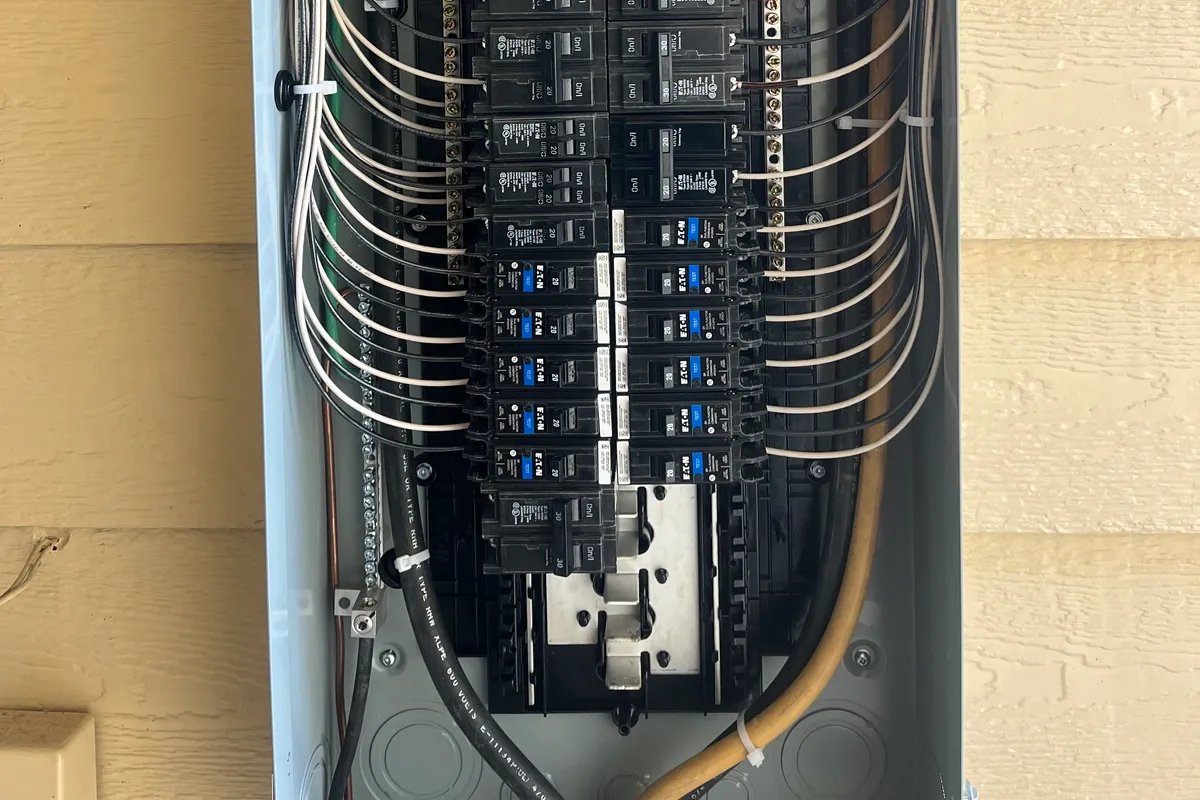 An open exterior main breaker panel on home siding with a surge protector and neatly bent, labeled circuit wiring.