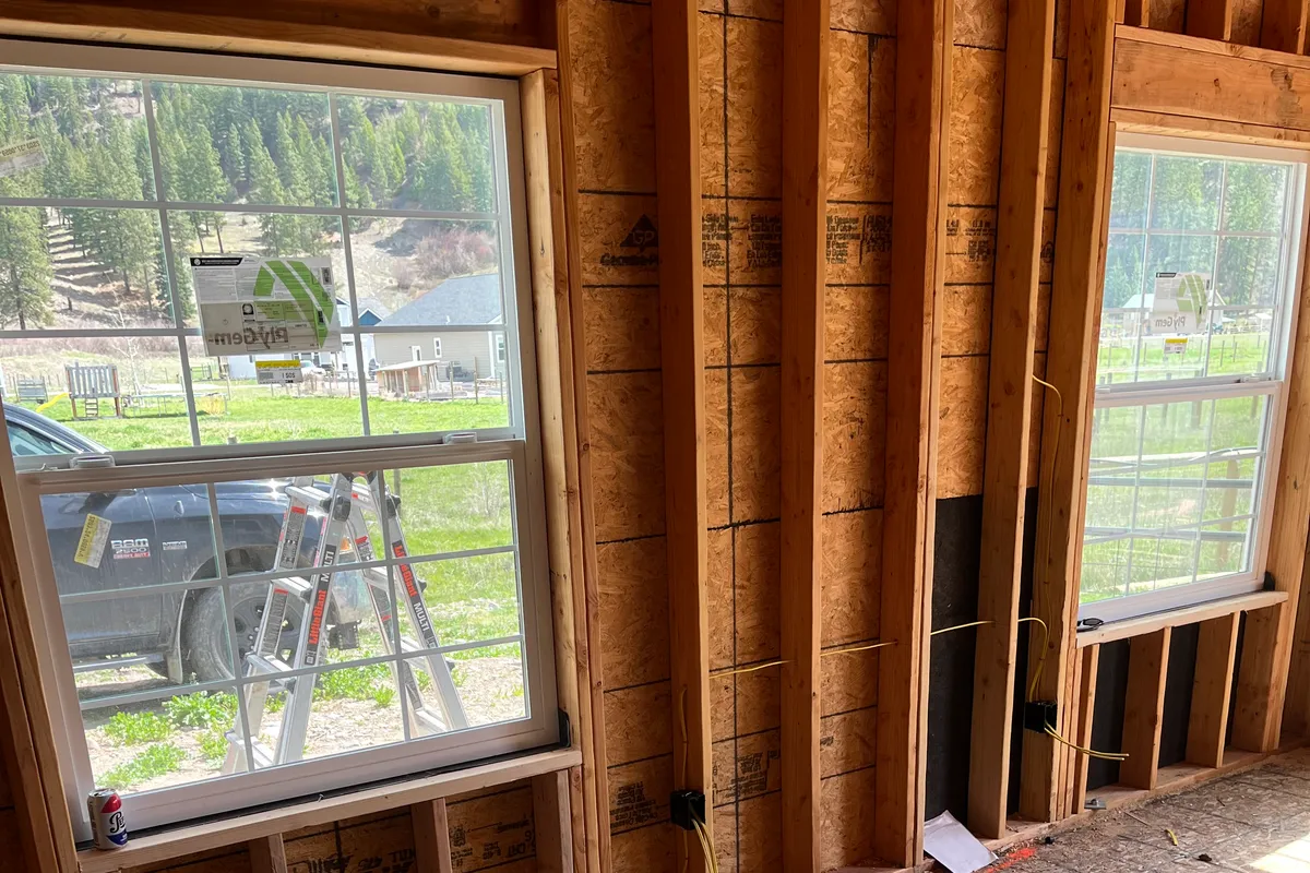 Wood-stud framing in a new home with yellow NM cable pulled to rough-in outlet boxes below the windows over an OSB subfloor.